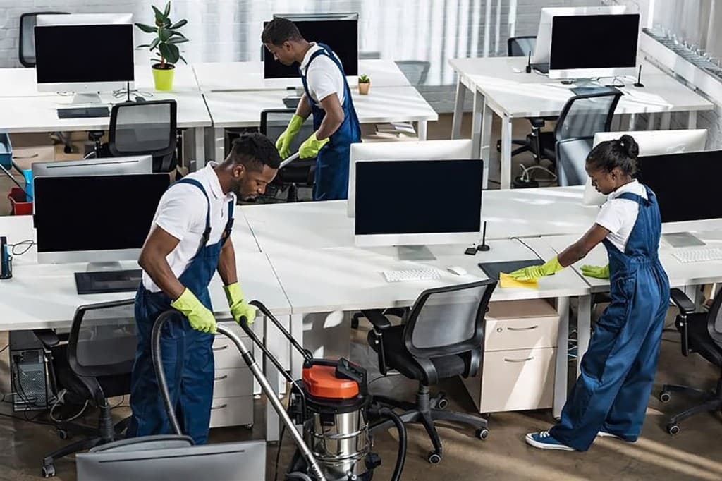 Professional cleaning team in navy overalls vacuuming and wiping desks in a bright modern office